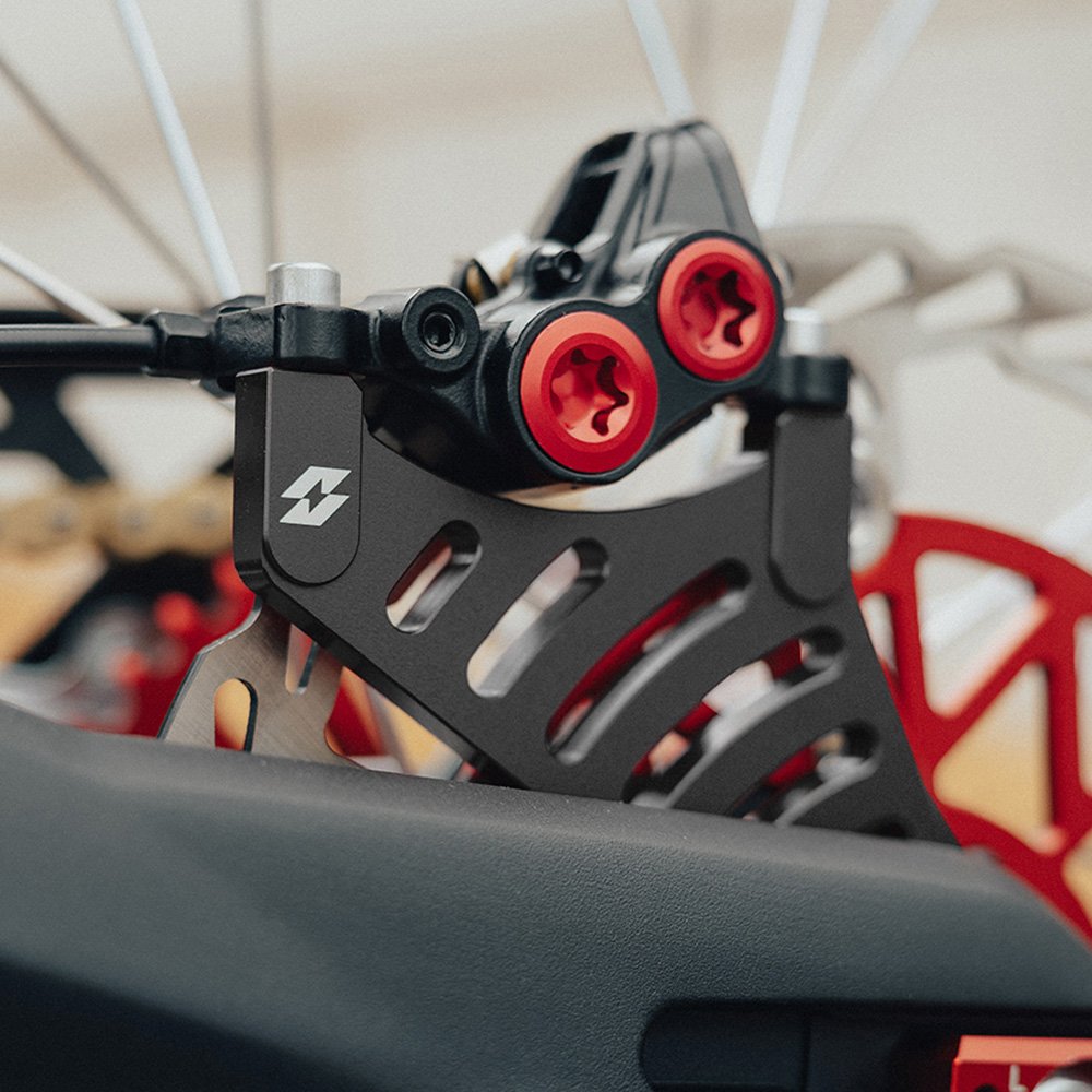 Black rear brake caliper bracket for Sur-Ron Light Bee and Talaria, fitted with a rear brake caliper