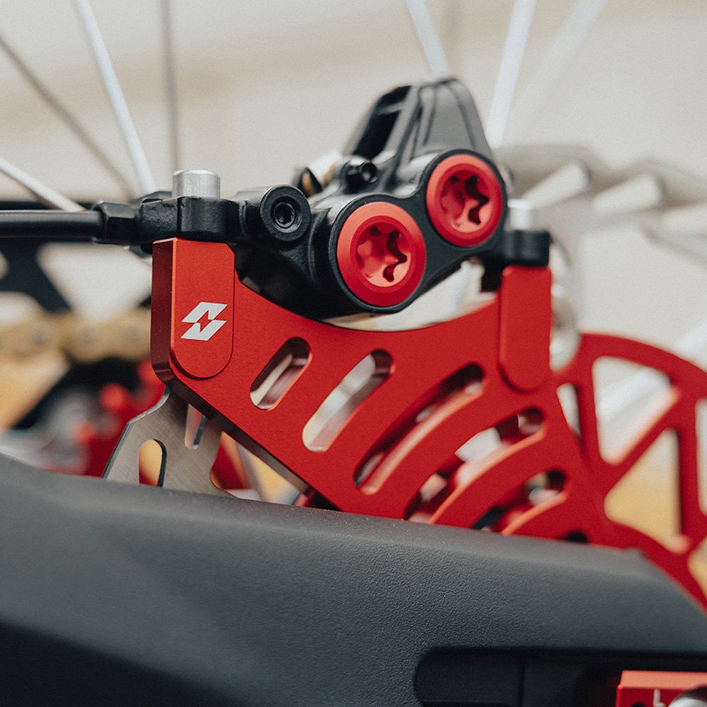 Red rear brake caliper bracket for Sur-Ron Light Bee and Talaria, fitted with a rear brake caliper